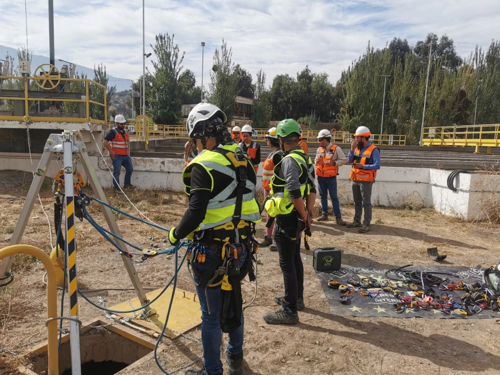 Dos trabajadores industriales con equipos de protección completos, incluyendo cascos y trajes protectores, suspendidos en el aire con arneses y cuerdas en una estructura industrial.