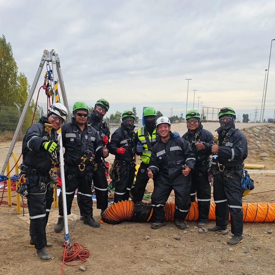 Un grupo de ocho trabajadores industriales al aire libre de Vertical Service, vistiendo trajes de seguridad negros con detalles reflectantes y cascos.